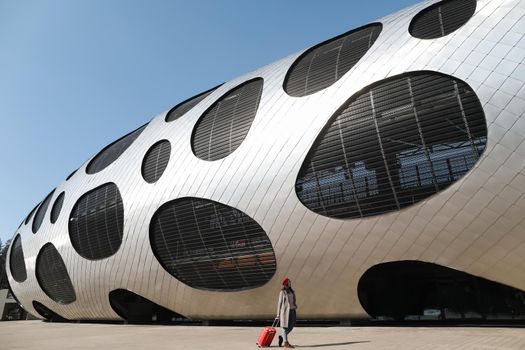 young woman with a red travel suitcase by the futuristic facade of modern architecture. Travel
