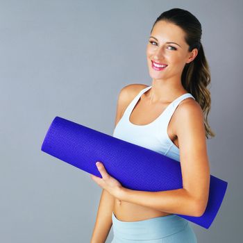 Cropped portrait of an attractive and sporty young woman carrying her yoga mat against a grey background.