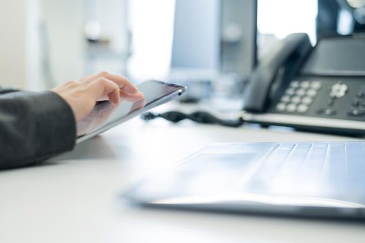 Close-up of the hands of a female secretary with a digital tablet. Faceless woman at her desk in the office