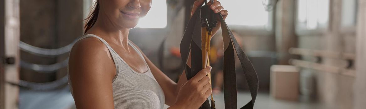 Portrait of attractive woman looking at camera and smile while working out with fitness straps in gym