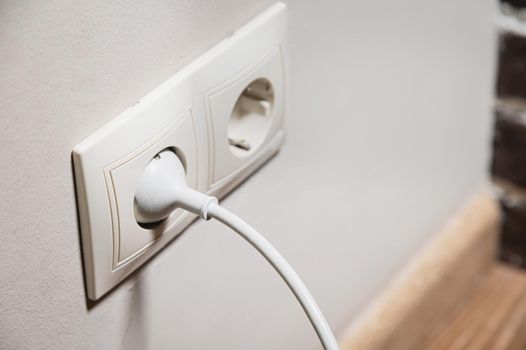 Close-up of a white electric plug in a 220 socket in the wall. Power on concept.