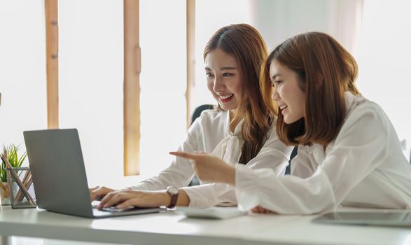 Two colleagues or students, asian girl are using a laptop while sitting at workplace discussing about job or education.