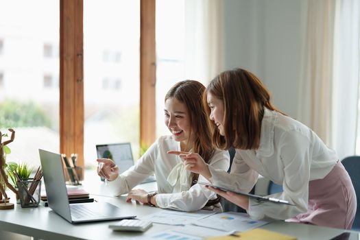 Two colleagues or students, asian girl are using a laptop while sitting at workplace discussing about job or education.