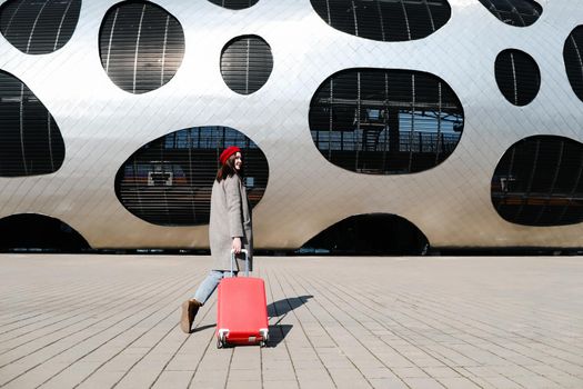 young woman with a red travel suitcase by the futuristic facade of modern architecture. Travel