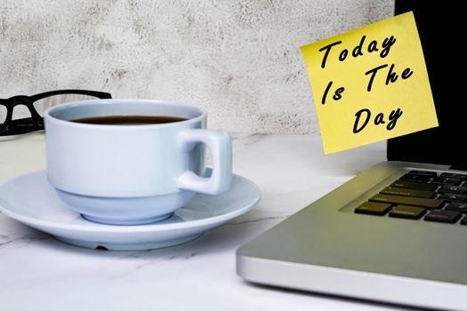 Inspirational quotes - Today is the day text on sticky note on a computer screen with other accessories and coffee on white table.