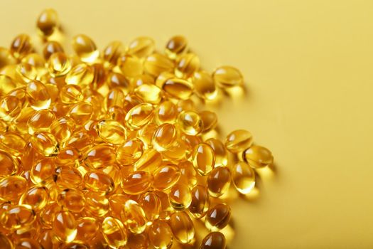 Pile of golden capsules of vitamin D3 on a yellow background with free space. Biologically active substances of the calciferol group are fat-soluble organic compounds.