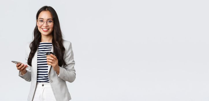 Business, finance and employment, female successful entrepreneurs concept. Professional asian businesswoman in glasses, having lunch, drinking takeaway coffee and using mobile phone.