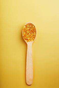 Vitamin D3 Capsules in a spoon with other vitamin D3 capsules around them on a yellow background. old capsules with a dietary supplement for joints teeth and bones. Close-up, free space