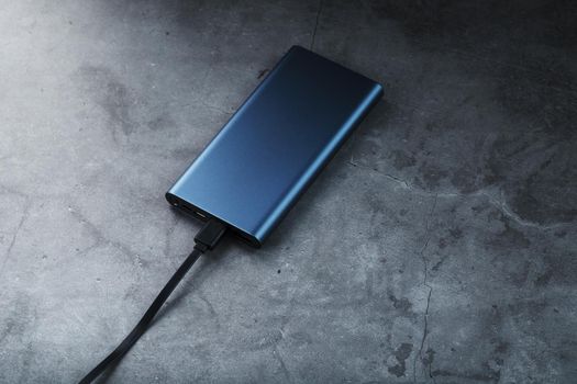 Portable External Battery Power Bank blue with USB Cord on a dark textured background for charging Gadgets