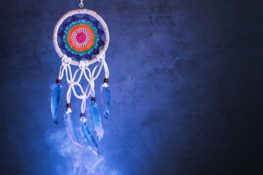 Dream catcher on a dark background with smoke and aquamarine light. Free space for text