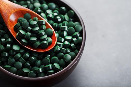 Vitamins from spirulina in a wooden cup with a wooden spoon on a dark background. Vegetarian source of amino acids and omega 3