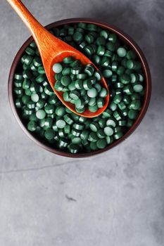 Vitamins from spirulina in a wooden cup with a wooden spoon on a dark background. Vegetarian source of amino acids and omega 3