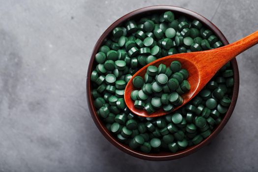 Vitamins from spirulina in a wooden cup with a wooden spoon on a dark background. Vegetarian source of amino acids and omega 3