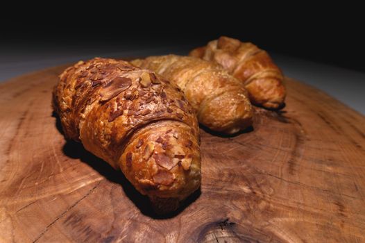 Close-up of a pile of three croissants on a wooden board against a dark background. Delicious and healthy breakfast.