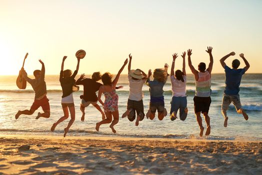 Rearview shot of a group of young friends jumping into the air at the beach.