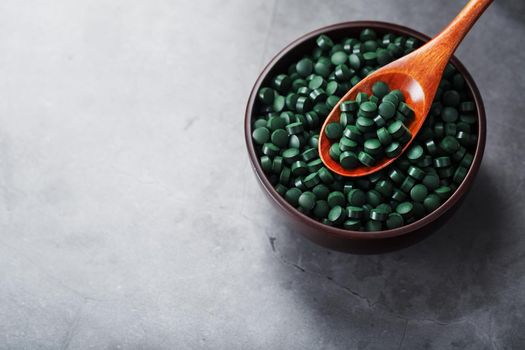 Organic spirulina tablets in a wooden cup with a wooden spoon on a dark background with free space top view