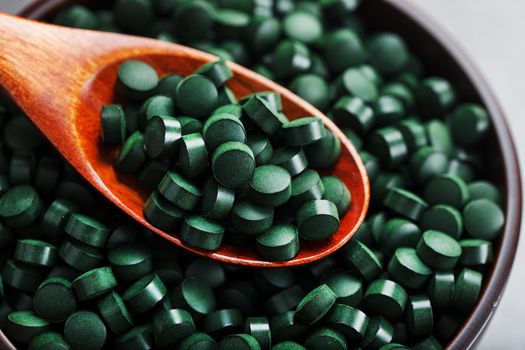 Organic spirulina tablets in a wooden cup with a wooden spoon on a dark background with free space top view