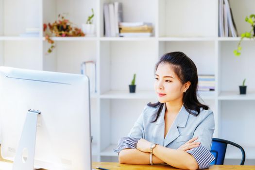 An Asian entrepreneur or businesswoman shows a smiling face while working with using computer on a wooden table