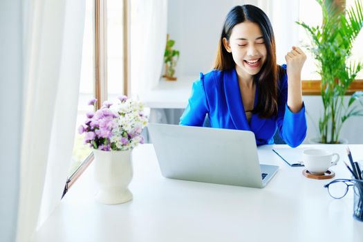 Business finance and investment, a business woman expresses happiness after successfully investing in the stock market on the Internet through a computer placed on a desk