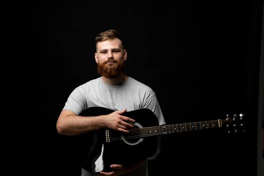 Portraite of bearded man musician, guitarist standing and holding a acoustic guitar in a hand and looks in a camera