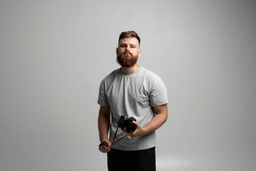 Portrait of bearded professional photographer with dslr camera looks straight into the camera isolated on gray background