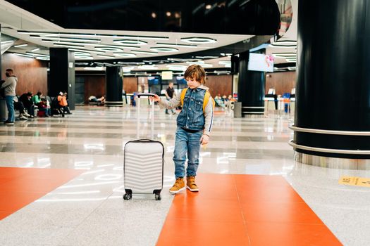 Child boy with backpack standing in the airport terminal, waiting for flight, travel with suitcase. Vacation concept.