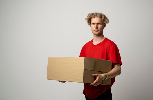 Delivery service. Happy young delivery man in red t-shirt standing with parcel isolated on white background