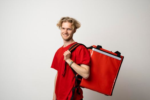 Delivery man employee man in a red tshirt uniform workwear work as a dealer courier and hold red thermal food bag backpack isolated on white background. Service concept