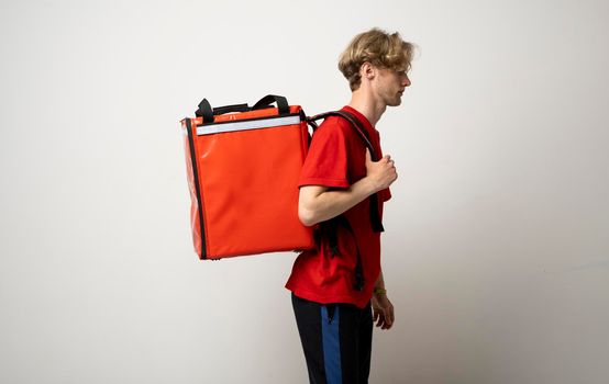 Delivery Service Cocnept. Portrait of male courier wearing red uniform and thermo backpack bag looking at camera isolated on white studio background