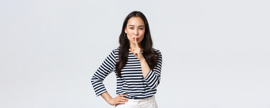 Lifestyle, people emotions and casual concept. Smiling cute asian girl asking keep secret, take promise not tell or be quiet about it, show shush sign, hush with finger over mouth, prepare surprise.