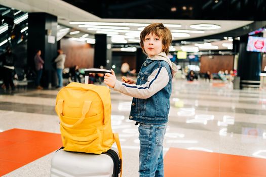 Child boy with backpack standing in the airport terminal, waiting for flight, travel with suitcase. Vacation concept.