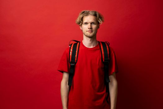 Portrait of happy smiling delivery man in a red t-shirt with thermal insulated bag on a shoulder looking in a camera. Food delivery service