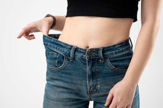 Woman in blue oversize jeans showing a result of weight loss on white background. Diet concept and weight loss