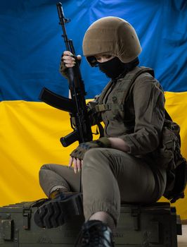 girl soldier with a Kalashnikov assault rifle on the background of the flag of Ukraine