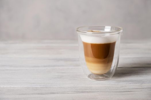 Heat-resistant double-walled glass cup stands on gray surface against gray background filled with latte or cappuccino. Hot coffee drink. Selective focus.