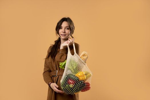 Beautiful attractive happy brunette woman holding mesh grocery bag with vegetables. Concept of no plastic. Zero waste, plastic free. Eco friendly concept. Sustainable lifestyle