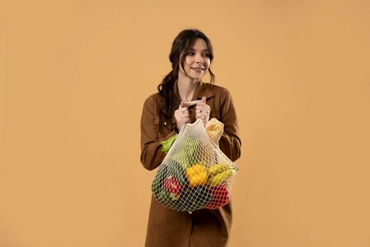 Zero waste, plastic free concept. Young brunette woman with cotton reusable mesh bag with fruits and vegatables. Shopping without plastic packaging in plastic free grocery store