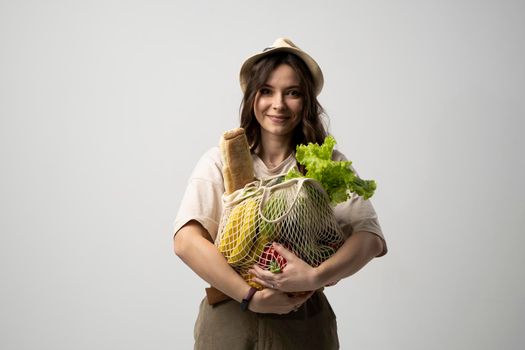 Portrait of happy smiling young woman in brown dress holding reusable string bag with groceries over orange background. Sustainability, eco living and people concept