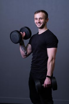 A guy with dumbbells in a black T-shirt muscular man background holding, from blue headphones from guy from athlete health, attractive t. Power biceps lifting, isolated young