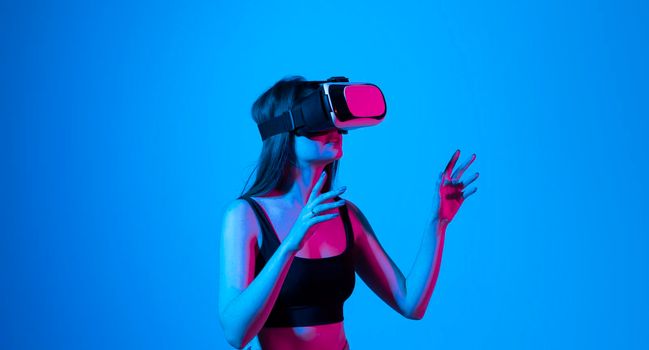 Portrait of young woman playing in VR-glasses in neon light on blue background. Concept modern gadgets and technologies. Future technology concept. Virtual reality gaming