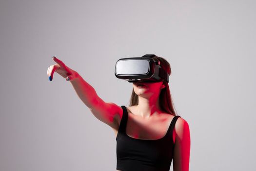 Brunette woman in a black t-shirt and VR headset looking up and trying to touch objects in virtual reality. VR is a technology that simulates a physical presence and to interact with environment