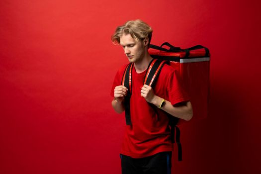 Young delivery employee man in red tshirt uniform with a thermal food bag backpack works as a courier in a food delivery service