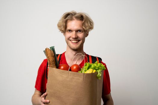 Delivery man employee in red t-shirt uniform hold craft paper packet with food isolated on white background studio