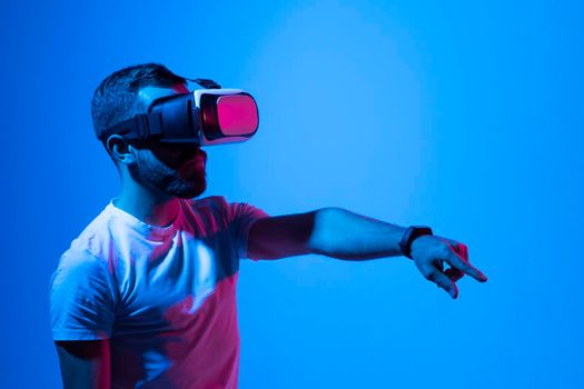 Portrait of man in black t-shirt wearing 3d headset glasses gesturing as if touching something what he doing in virtual reality while playing video games. Metaverse