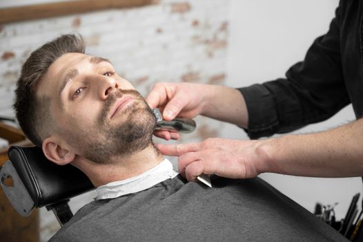 Professional barber cutting beard of handsome man. High quality photography.