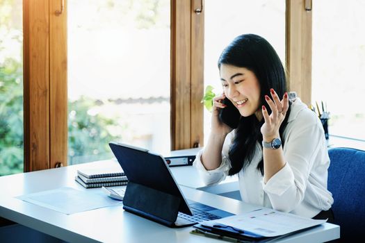 A female entrepreneur or businesswoman shows a smiling face while using smartphone and tablet computer for video conference working on a wooden table