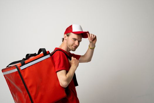 Side view delivery employee man 20s in red cap t-shirt uniform thermal food bag backpack work courier service