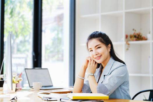 An Asian entrepreneur or businesswoman shows a smiling face while working with using computer on a wooden table