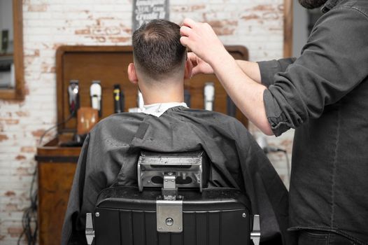 Barber cutting hair with scissors to a handsome young man . High quality photography
