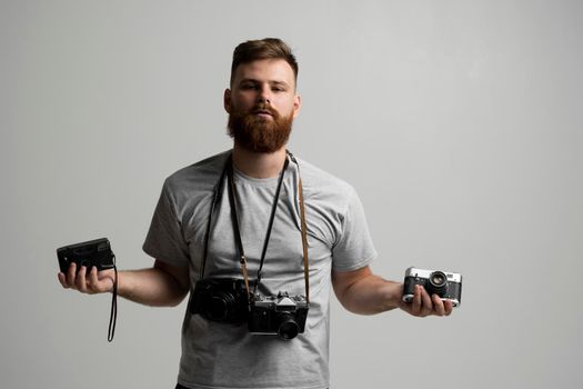 Portraite of professional handsome bearded male photographer with bunch of vintage photo cameras in photo studio, isolated on white background